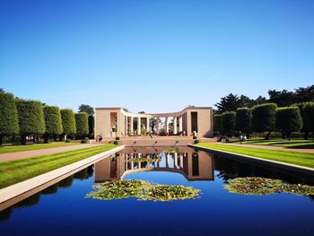 Reflection of building in lake against clear blue sky