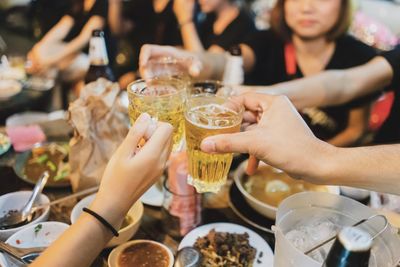 Cropped friends toasting beer glasses at restaurant