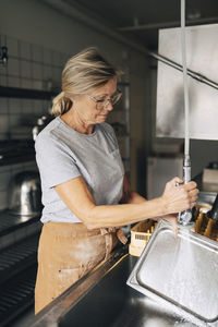 Senior female baker spraying water on tray while working in commercial kitchen