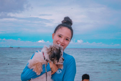 Portrait of young woman standing at beach against sky