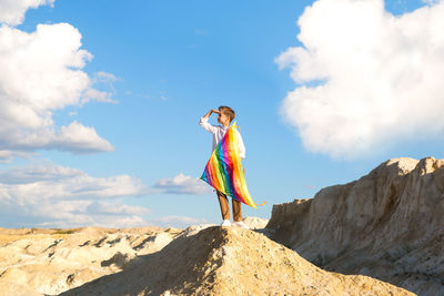 A 9-year-old boy with a bright colorful kite stands high on a mountain against a background 