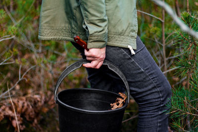 Woman picking mushrooms in forest.  woman holding a black bucket and a knife in the forest. mushroom 
