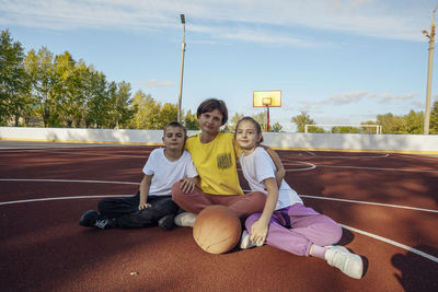 Outdoor hugs,  mother and teenage children cuddle gently in the sun on basketball court