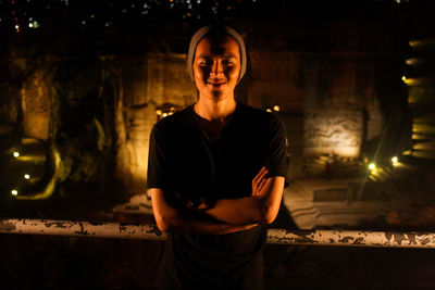 Portrait of young man standing against illuminated wall at night