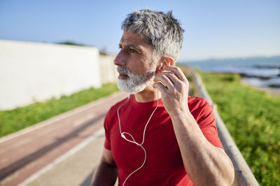 Mature man with earphones looking away by the sea