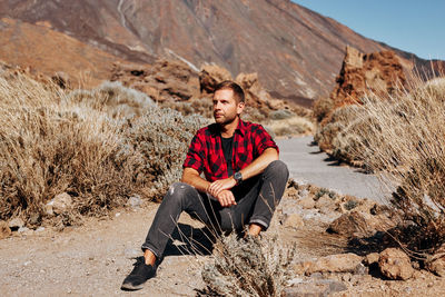 Man looking away while sitting on rock