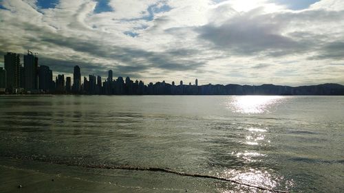 City at waterfront against cloudy sky