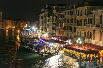 Illuminated boats moored in canal amidst buildings in city at night