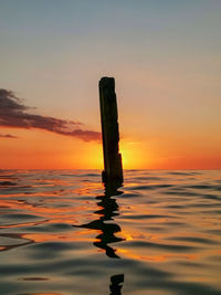 Wooden post in sea against sky during sunset