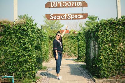 Full length of woman pointing at information sign while standing against plants