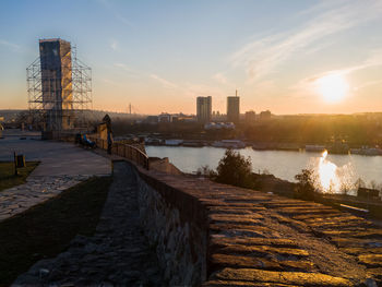 Bridge over river by buildings in city against sky during sunset