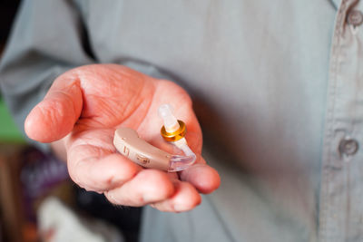 Midsection of man holding hearing aid