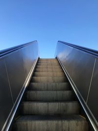 Low angle view of escalator against clear blue sky