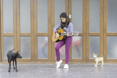 Full length of girl playing guitar while standing with dogs against wall