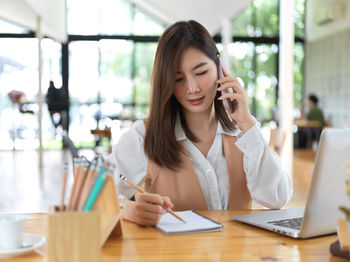 Smiling businesswoman talking on phone sitting at cafe