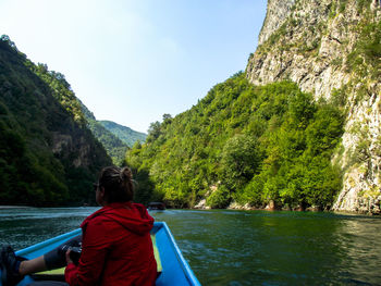 Full length of woman sitting on boat in river amidst mountains