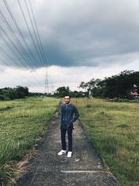 Man standing on footpath amidst grassy field against cloudy sky