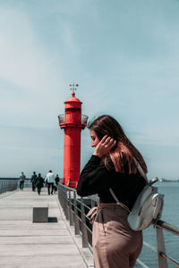 Woman standing by lighthouse on pier against sky