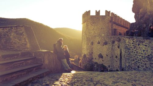 Tourists visiting castle by mountain against clear sky at morning