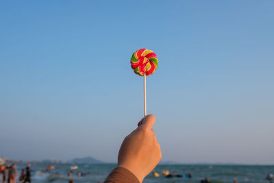 Cropped hand of woman holding lollipop at beach against clear sky