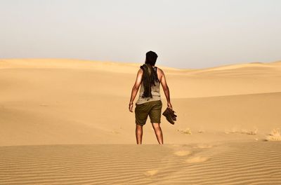 Rear view of man walking in desert against clear sky