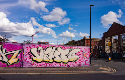 Graffiti on wall by street against sky in city