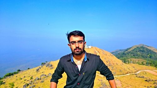 Portrait of young man wearing sunglasses standing against mountain