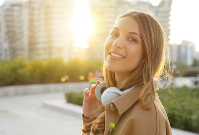 Young woman takes off her headphones and smiles on camera relaxing outdoor at sunset