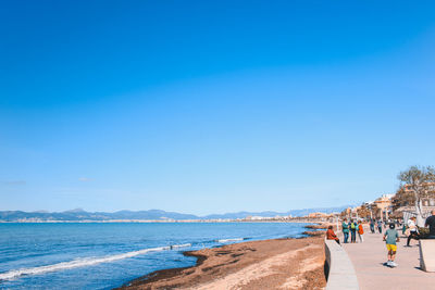 People on beach against clear blue sky