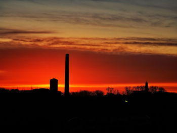 Silhouette factory against sky during sunset