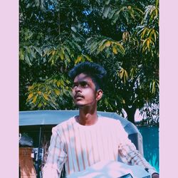 Young man looking away while standing by tree