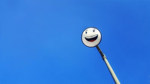 Low angle view of anthropomorphic smiley face on street light against clear blue sky