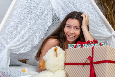 Portrait of smiling young woman lying on bed with gift box at home