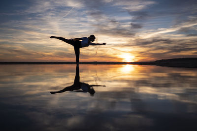 Silhouette person in sea against sky during sunset