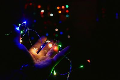 Cropped hand of person holding illuminated string light at night