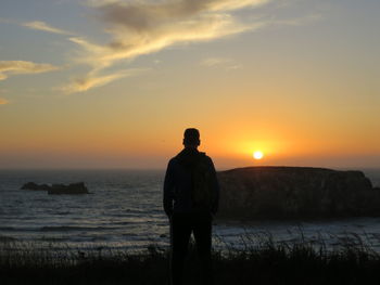 Rear view of man looking at sea against sky during sunset