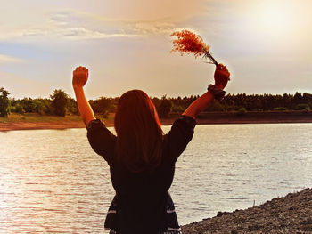 Rear view of woman with arms raised against sky during sunset