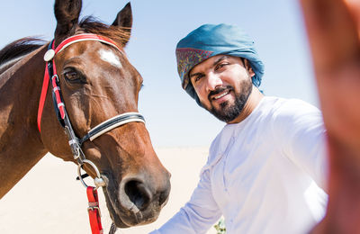 Portrait of smiling man with horse against clear sky