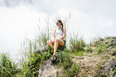 Young woman sitting on land against sky