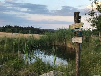 Wooden posts on field by lake against sky