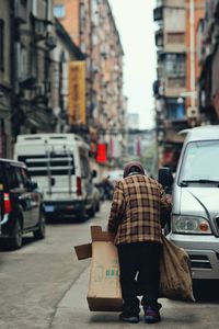 Rear view of woman carrying box and sack while walking on street