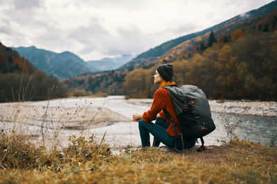 Rear view of woman sitting on mountain against sky