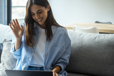 Young woman using laptop while sitting on sofa at home