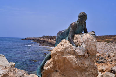 Statue on rock by sea against clear blue sky