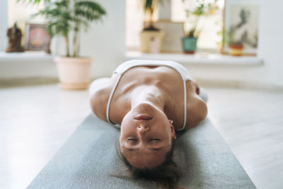 Young fit woman practice yoga doing asana in light yoga studio with green house plants