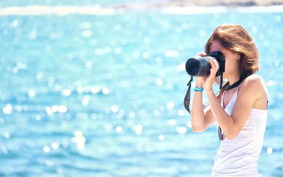 Woman photographing while standing by sea