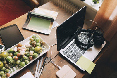 High angle view of laptop with headphones by tomatoes in tray on table at home