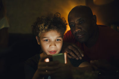 Boy using smart phone by father in living room at night