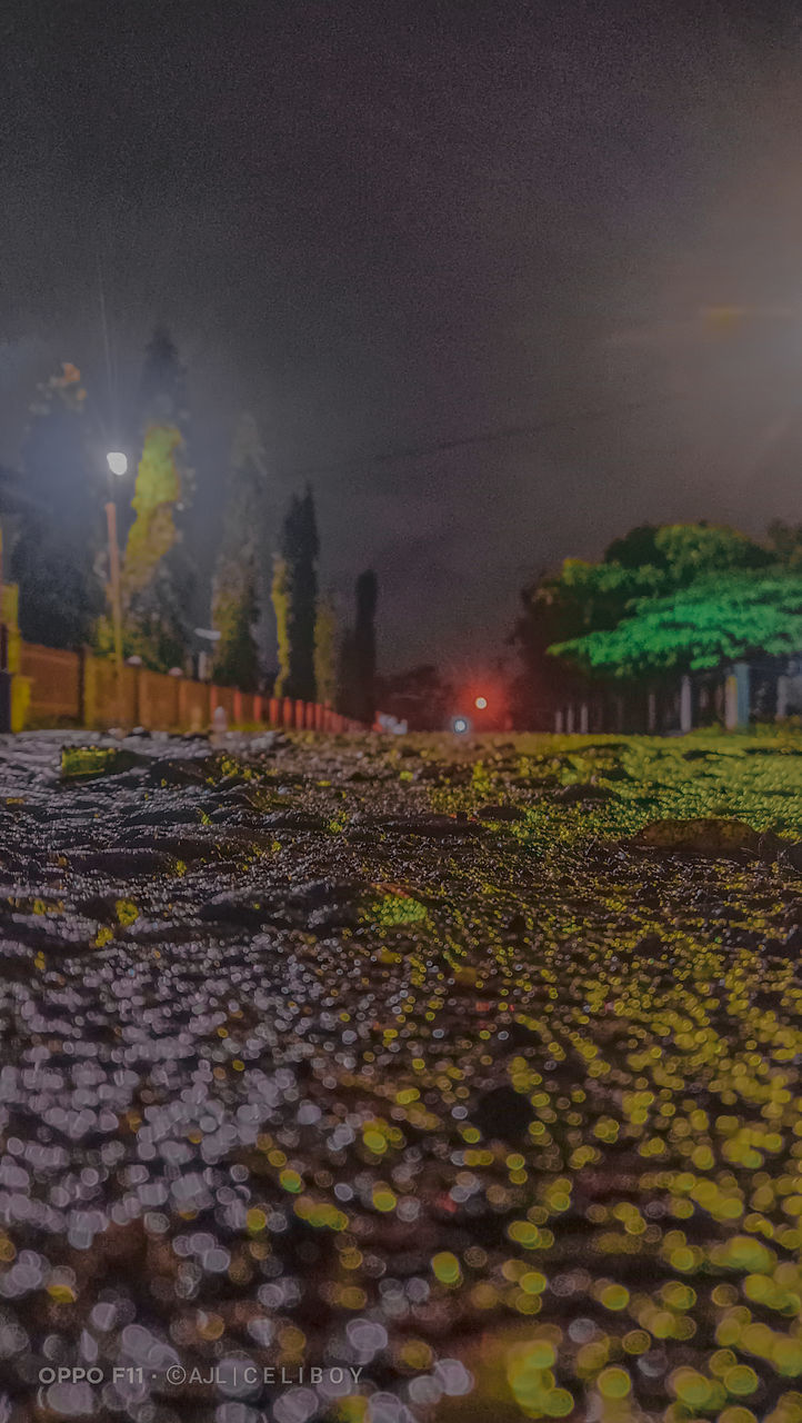 SURFACE LEVEL OF FOOTPATH BY ILLUMINATED STREET AGAINST SKY