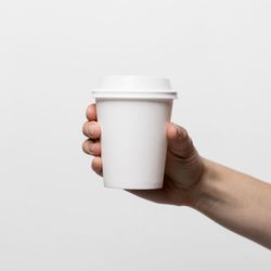 Close-up of hand holding coffee cup against white background